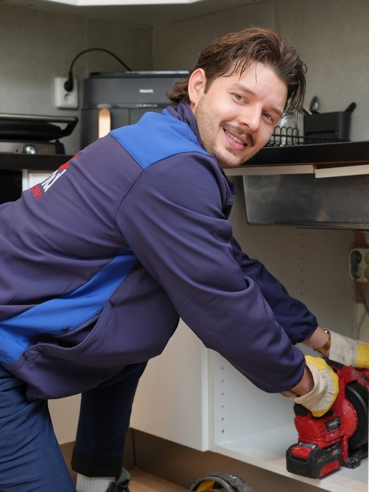 Loodgieter van Holland Loodgieters aan het werk onder een keukenaanrecht in Den Haag met professioneel gereedschap
